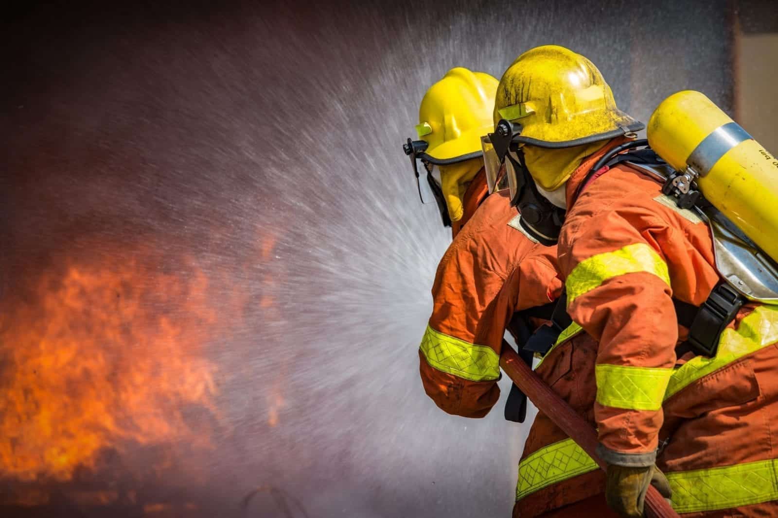 Two firefighters spray water from a hose at a nearby fire.