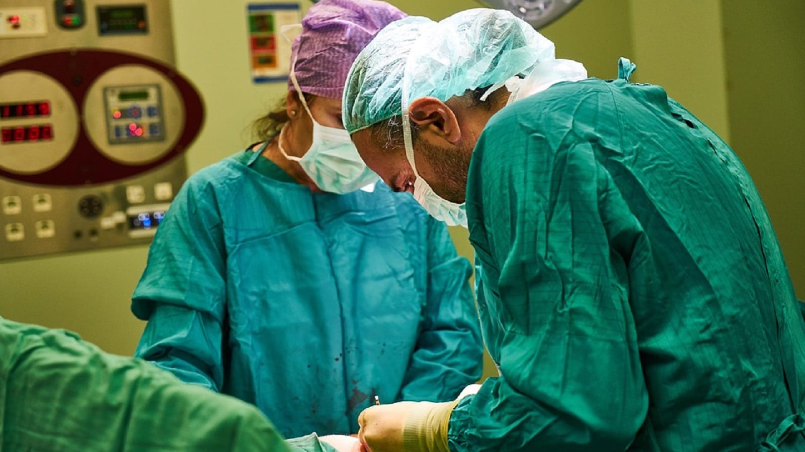 Two surgeons wearing surgical gowns, caps, and masks perform a procedure in an operating room.