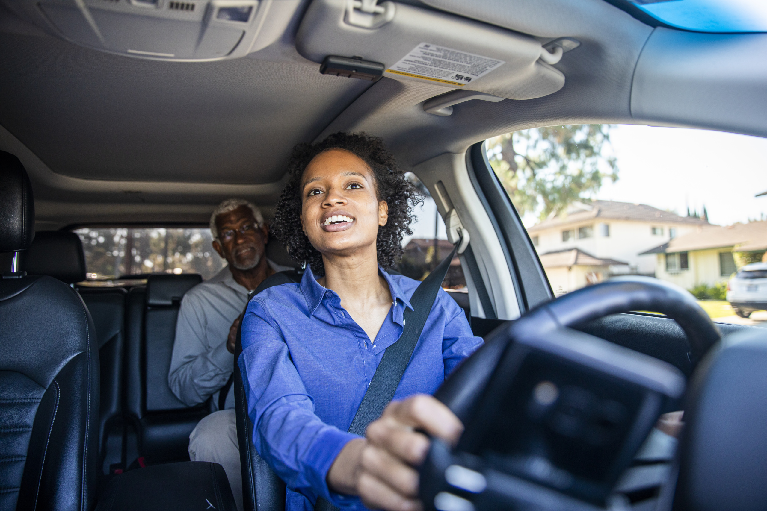 A rideshare driver converses with her passenger while looking in the rearview mirror.