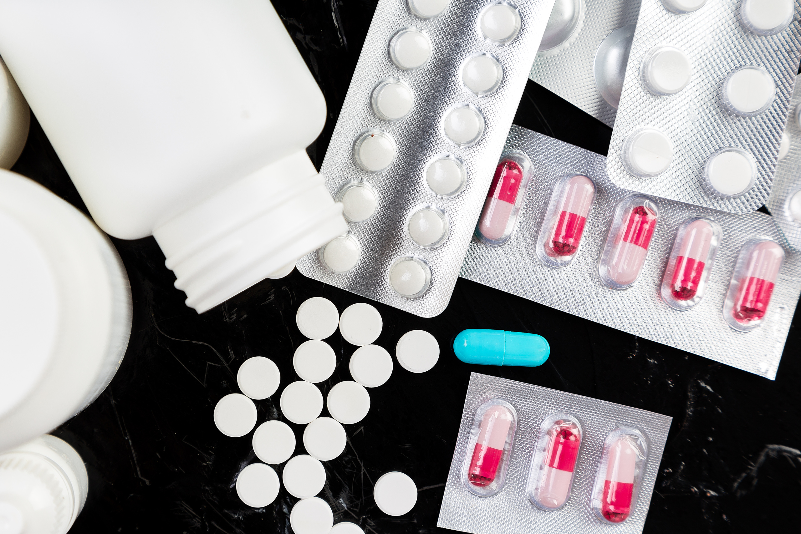 A variety of prescription pills and pill bottles displayed on a black surface.